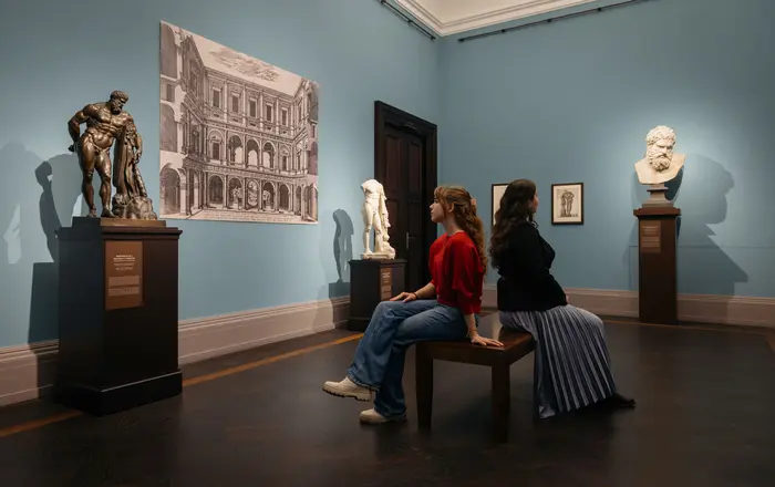 Raumansicht mit zwei Frauen auf einer Bank, die sich ein Bild anschauen