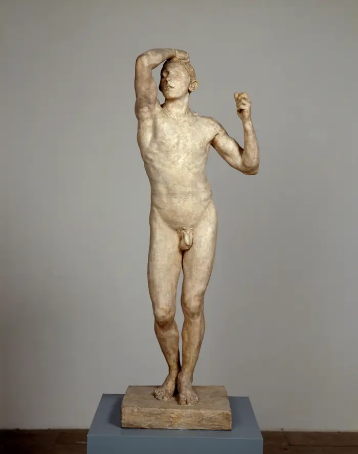 Skulptur eines nackten Mannes, eine Hand am Kopf