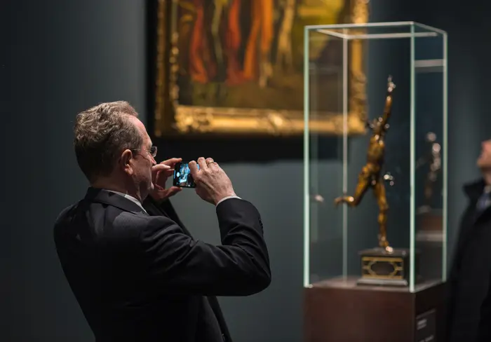 Ein Besucher fotografiert mit einem Smartphone eine Bronzefigur 