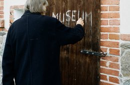 Inge Mahn vor ihrem Scheunenmuseum in Groß Fredenwalde Frau in Rückenansicht schreibt mit Kreide "Museum" auf ein Scheunentor
