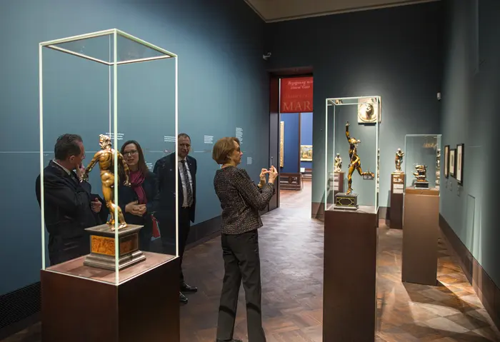 Besucherinnen und Besucher diskutieren über eine Bronzestatue in einem Ausstellungsraum